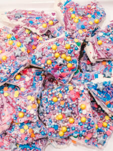 white, pink, purple and blue candy bark with colored sprinkles on top sitting on a white plate