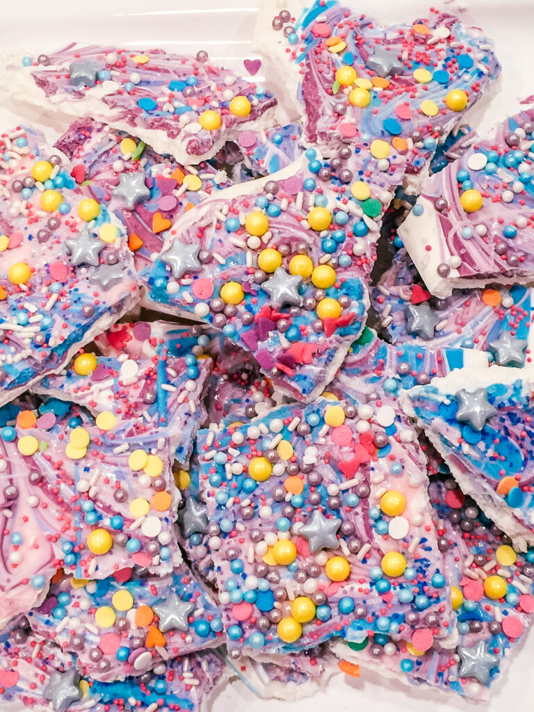 white, pink, purple and blue candy bark with colored sprinkles on top sitting on a white plate