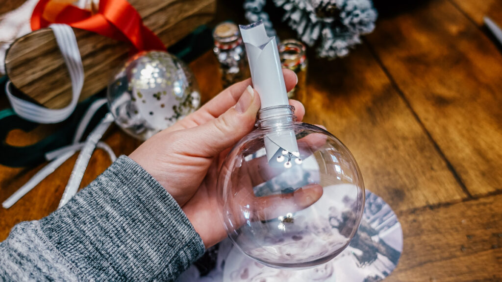 rolled photo being put into a clear ornament
