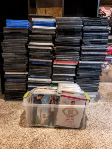 empty DVD cases stacked on the floor with a clear tub of DVDs sitting in front of them