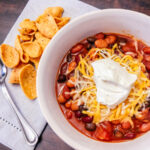 bean chili in a white bowl with shredded cheese and sour cream on top