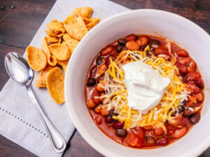 bean chili in a white bowl with shredded cheese and sour cream on top