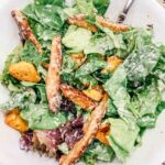 salad in a white bowl with caesar dressing on top