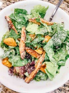 salad in a white bowl with caesar dressing on top