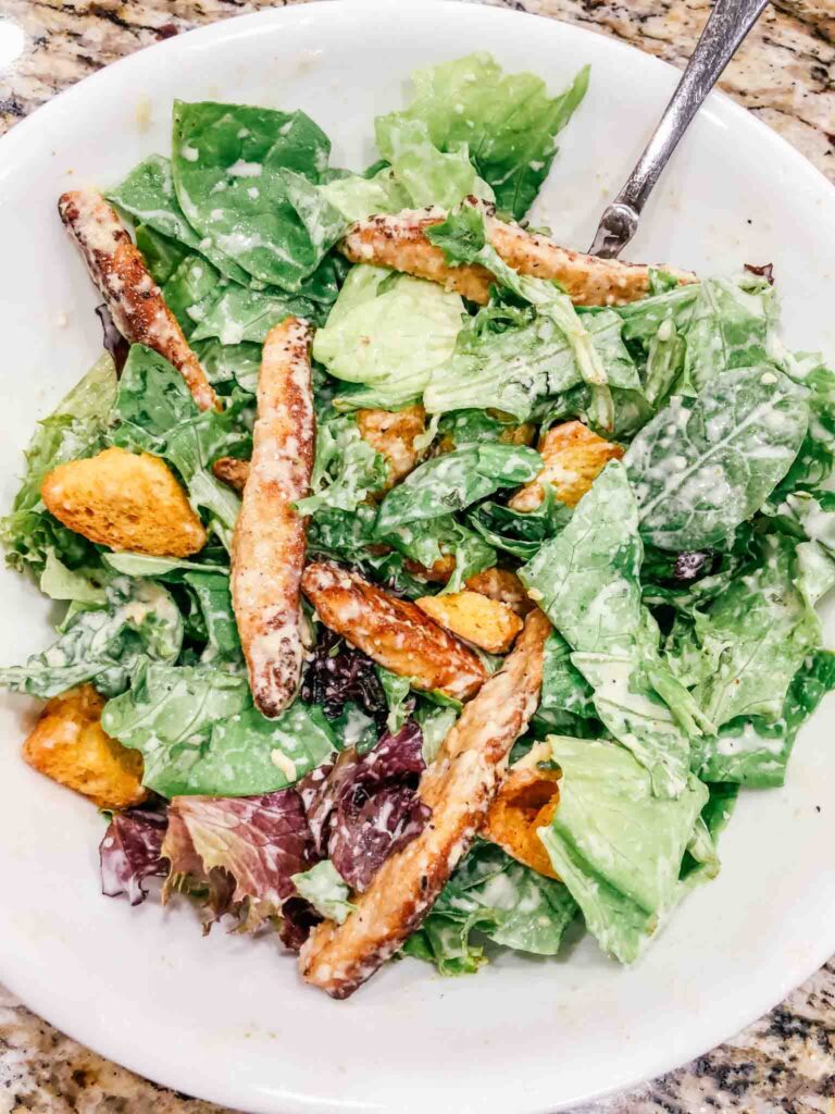 salad in a white bowl with caesar dressing on top